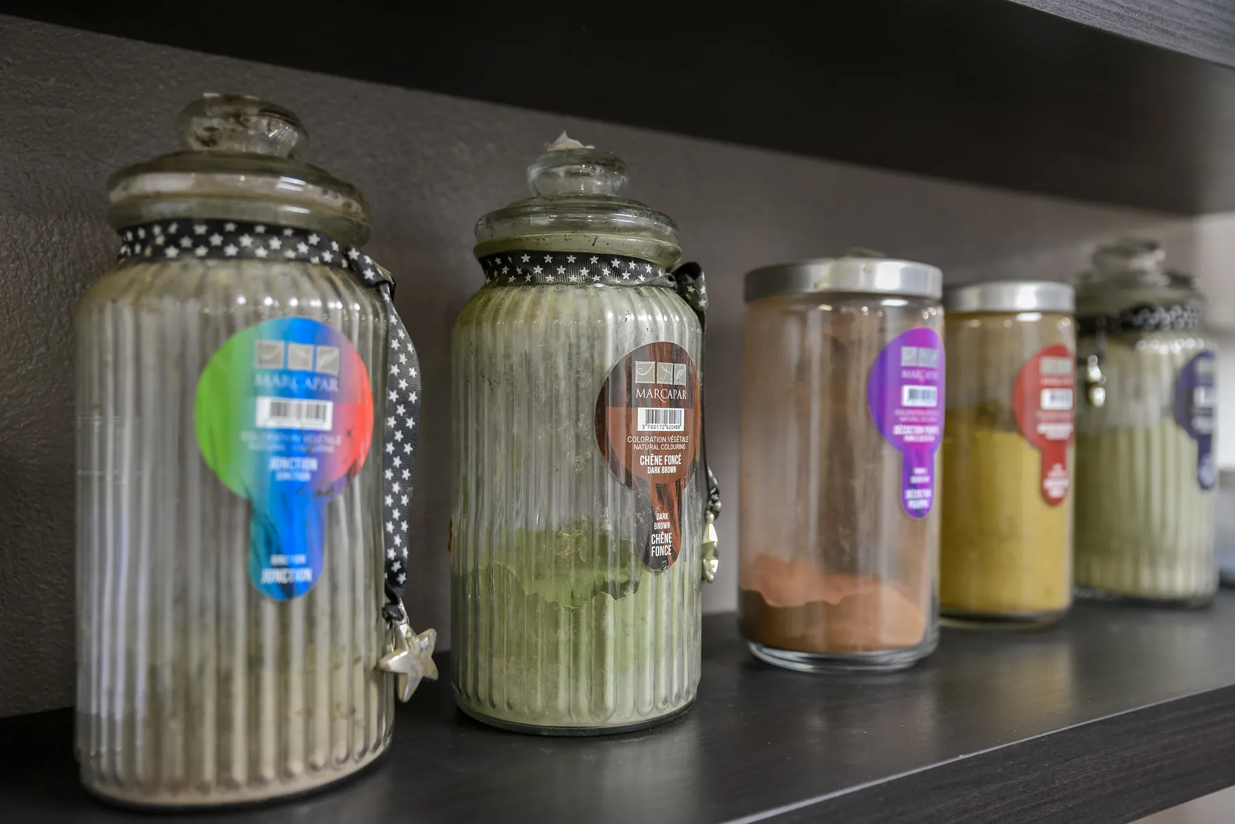 Les bocaux de poudres végétales Marcapar sur l’étagère du salon, en vert, brun et ocre